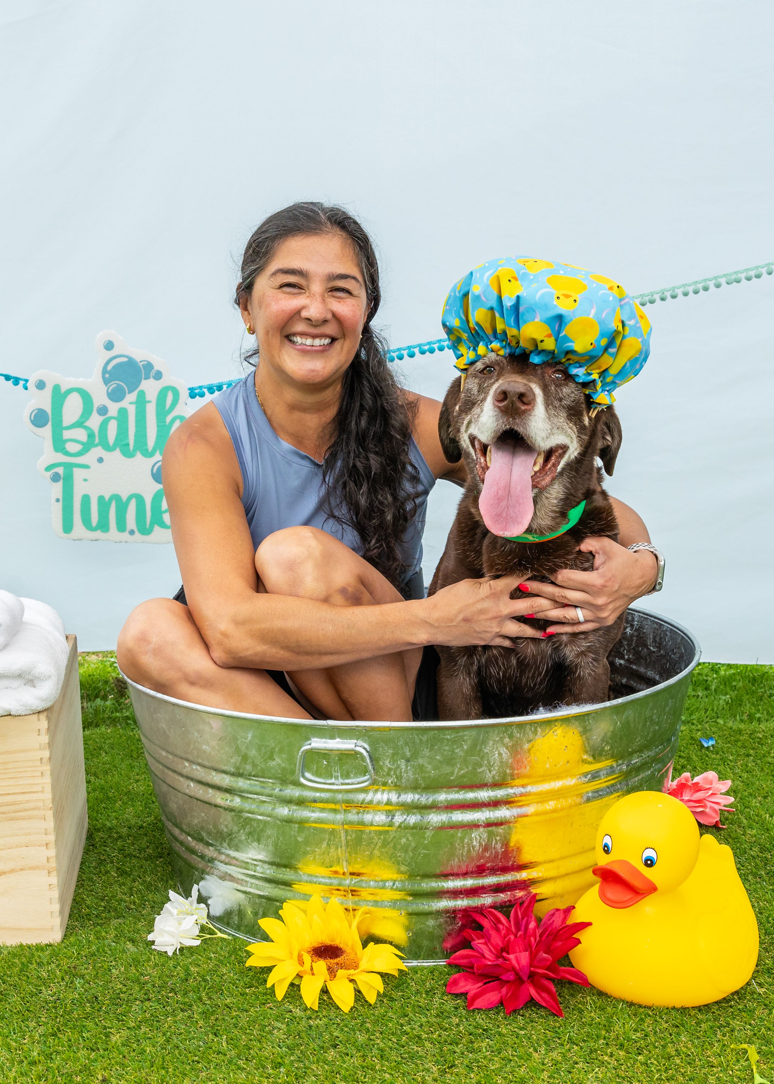 Happy dog getting bathed in metal tub with rubber duck and flower decorations.