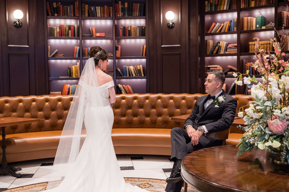A unique wedding portrait captured in a cozy library setting with leather seating and illuminated bookshelves.