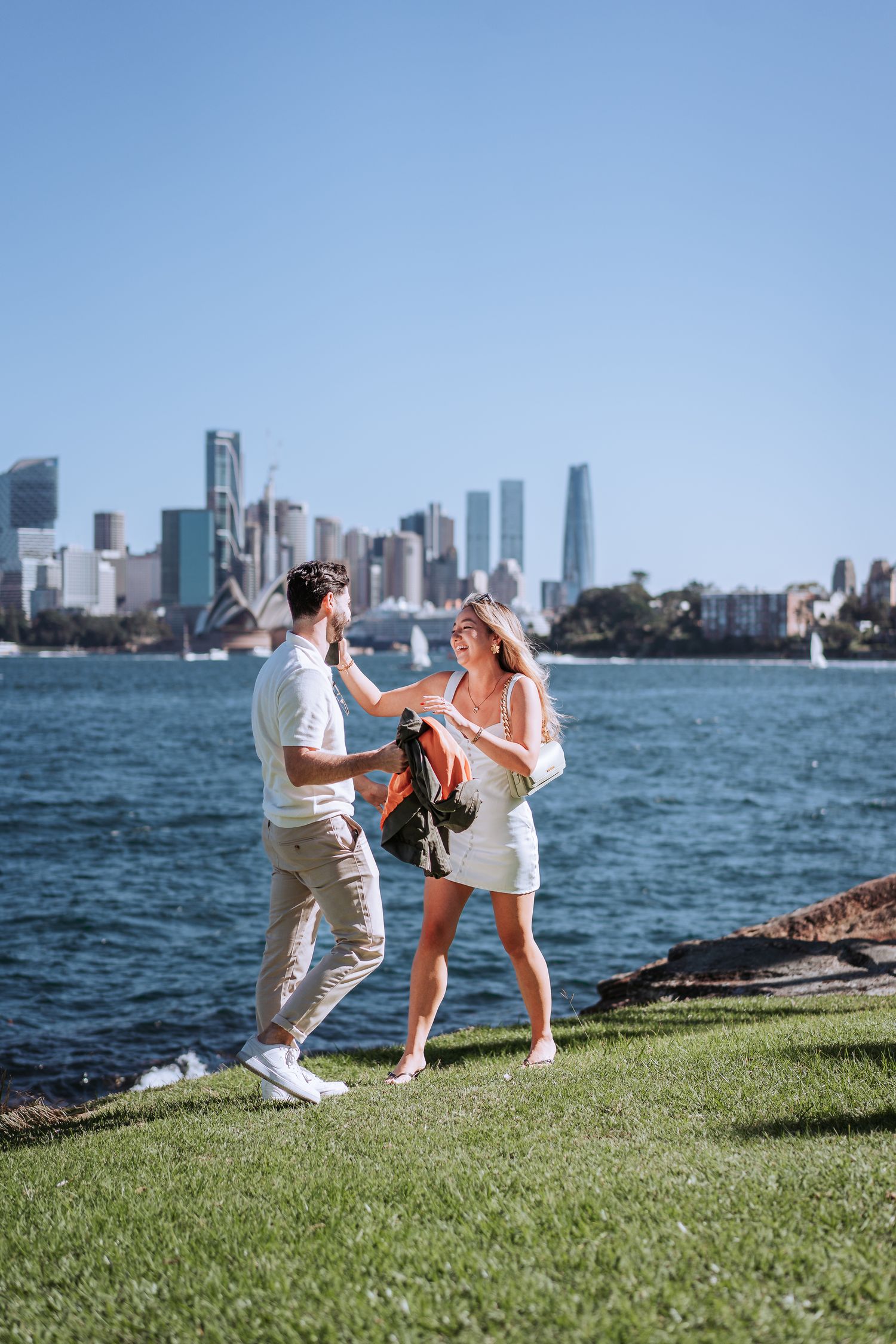 A couple shares a romantic moment by the water with the Sydney skyline in the background.