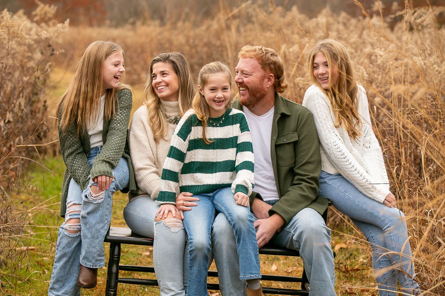 Family sitting together on wooden bench surrounded by autumn foliage.