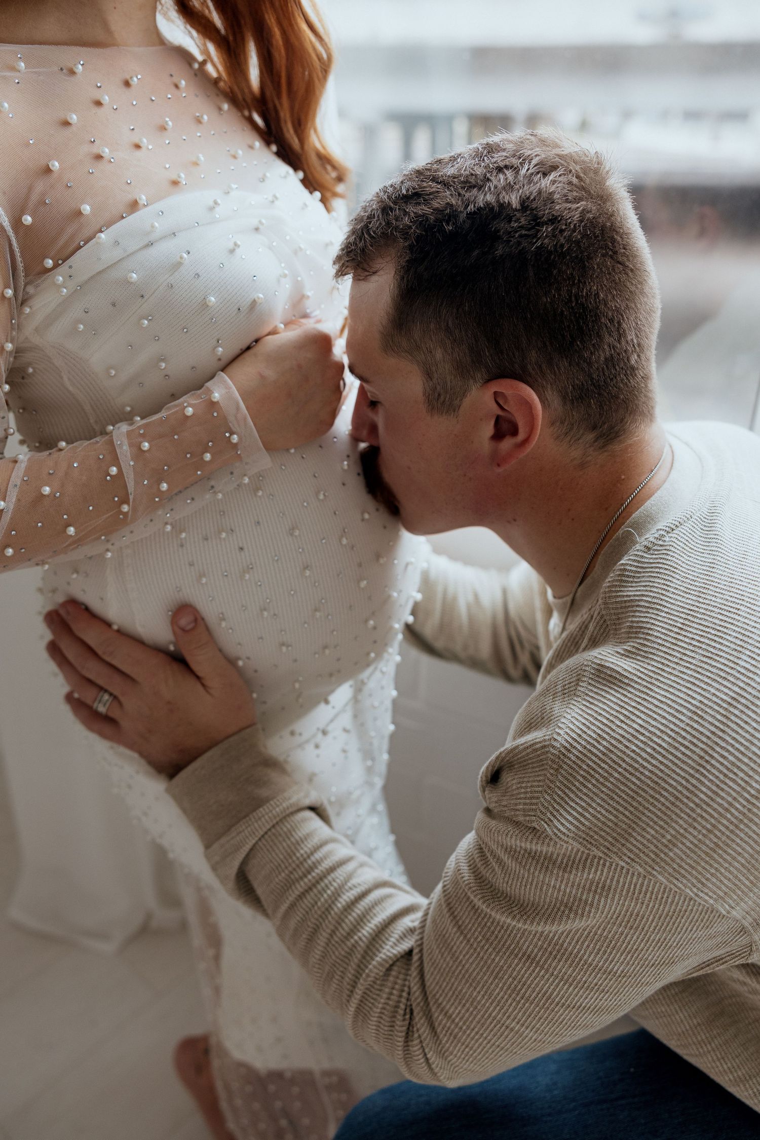A tender moment of a couple expecting a baby, with the partner gently kissing the pregnant belly.