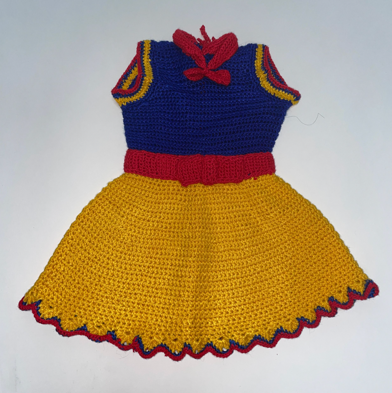 Crocheted yellow, blue and red princess-inspired dress with scalloped hem displayed on white background.
