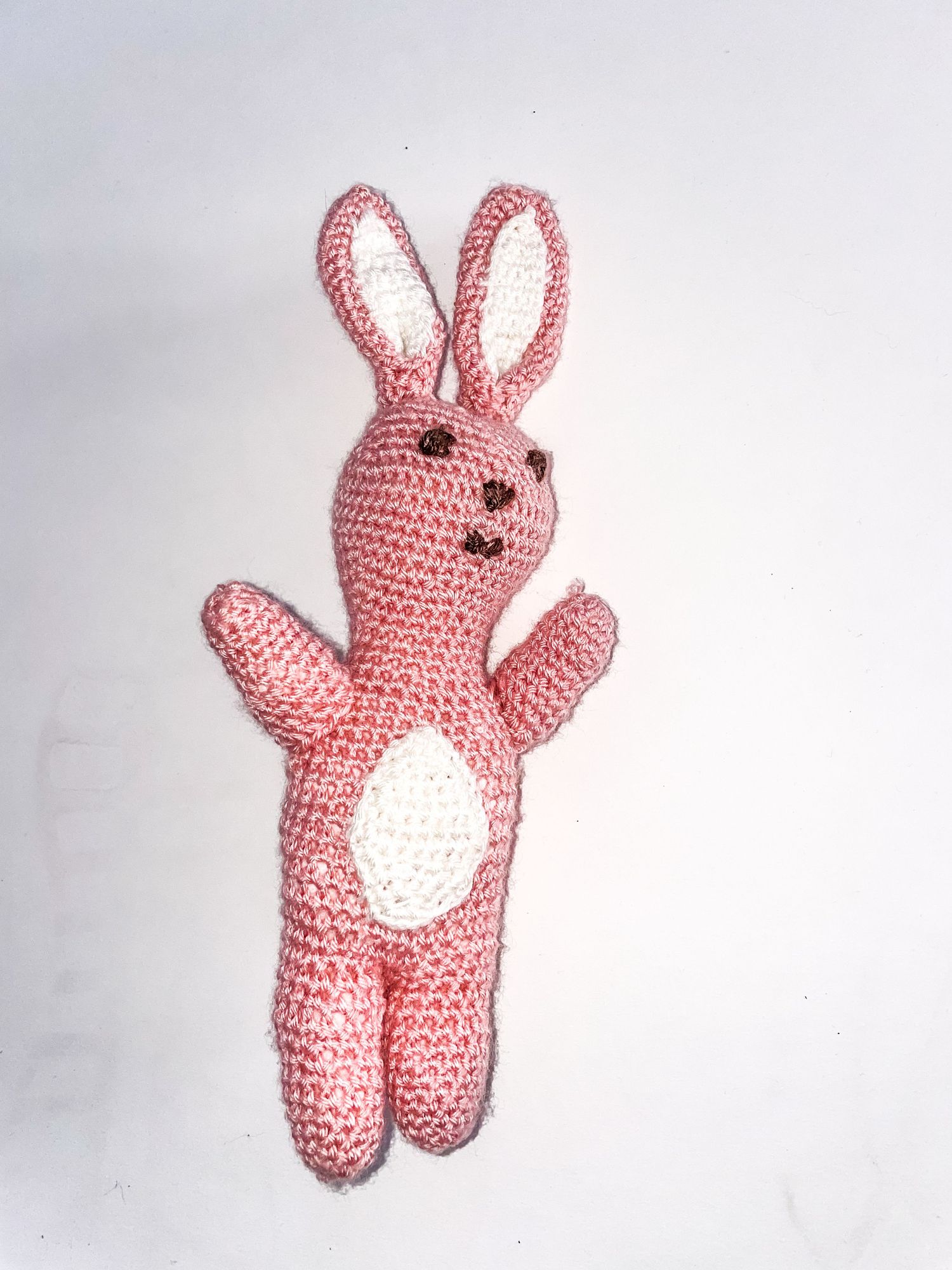 Pink crocheted bunny amigurumi with white belly patch shown in different poses.