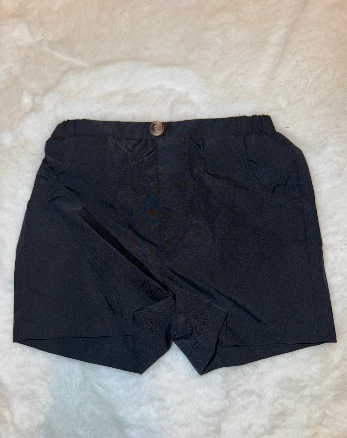 Black casual shorts with button closure displayed on white fabric.