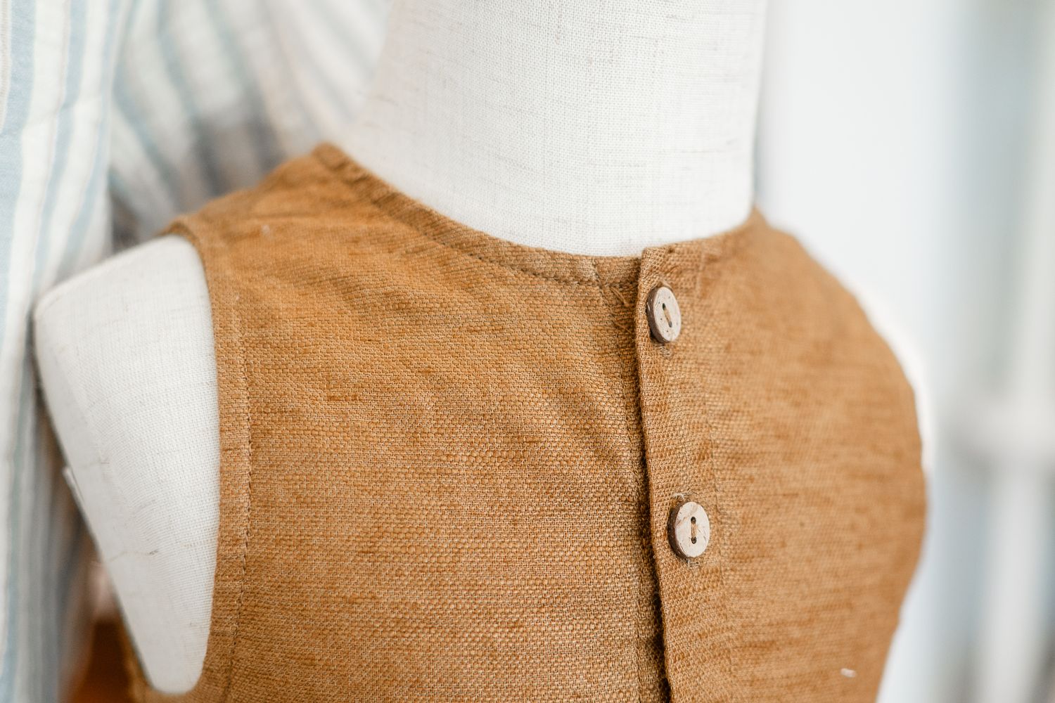 Close-up view of a camel-colored linen garment with white buttons displayed on a mannequin.