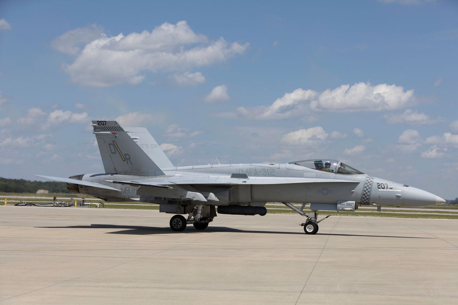 An F/A-18 Hornet military fighter jet parked on a runway under blue skies with white clouds.