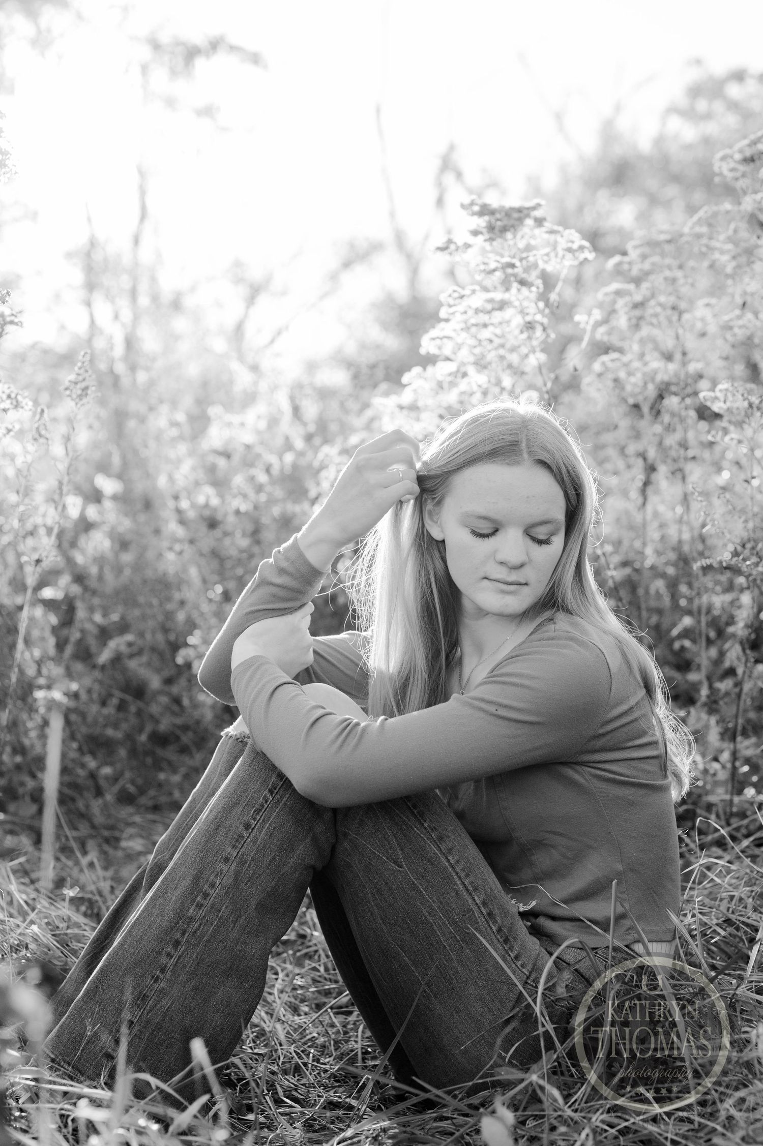 Black and white photo showing relaxed pose among wild grasses with natural lighting.