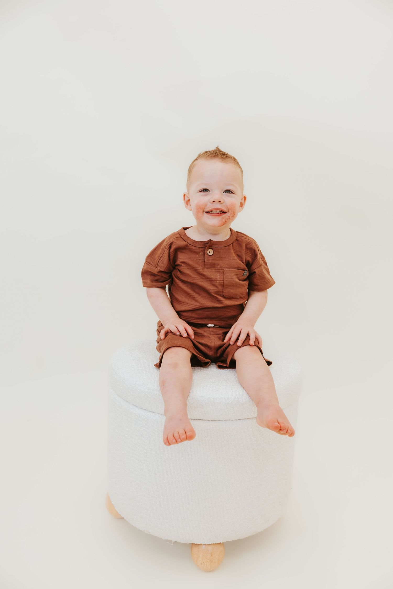 A cheerful pose on a white ottoman wearing brown casual attire.