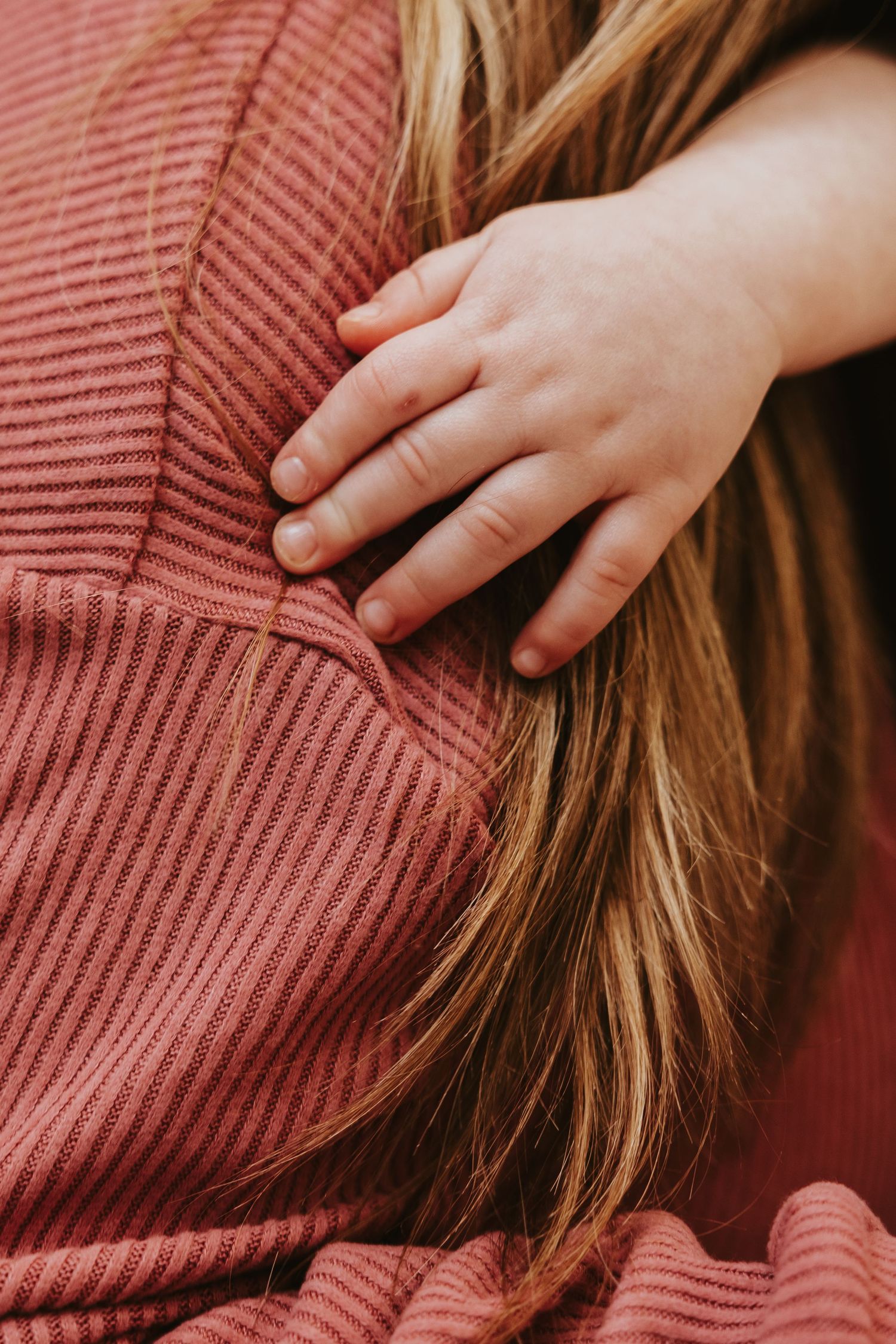 Close-up of a small hand touching red corduroy fabric with long hair visible.