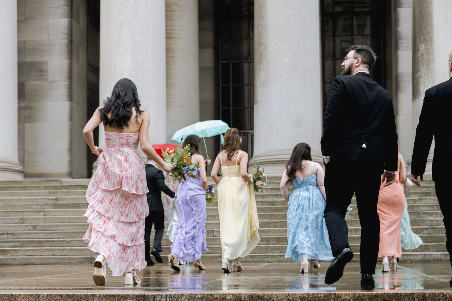 A group of people in colorful dresses walk up stone steps while carrying umbrellas on a rainy day.