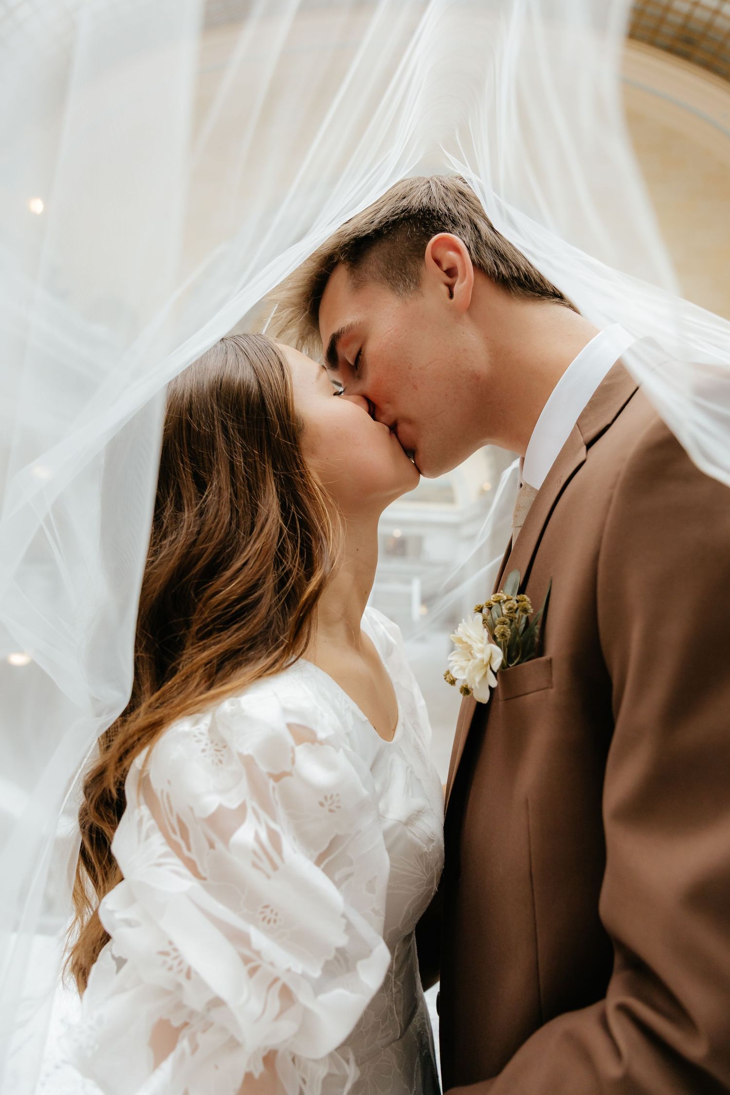 Bride and groom share a romantic kiss beneath a flowing white veil at their wedding.