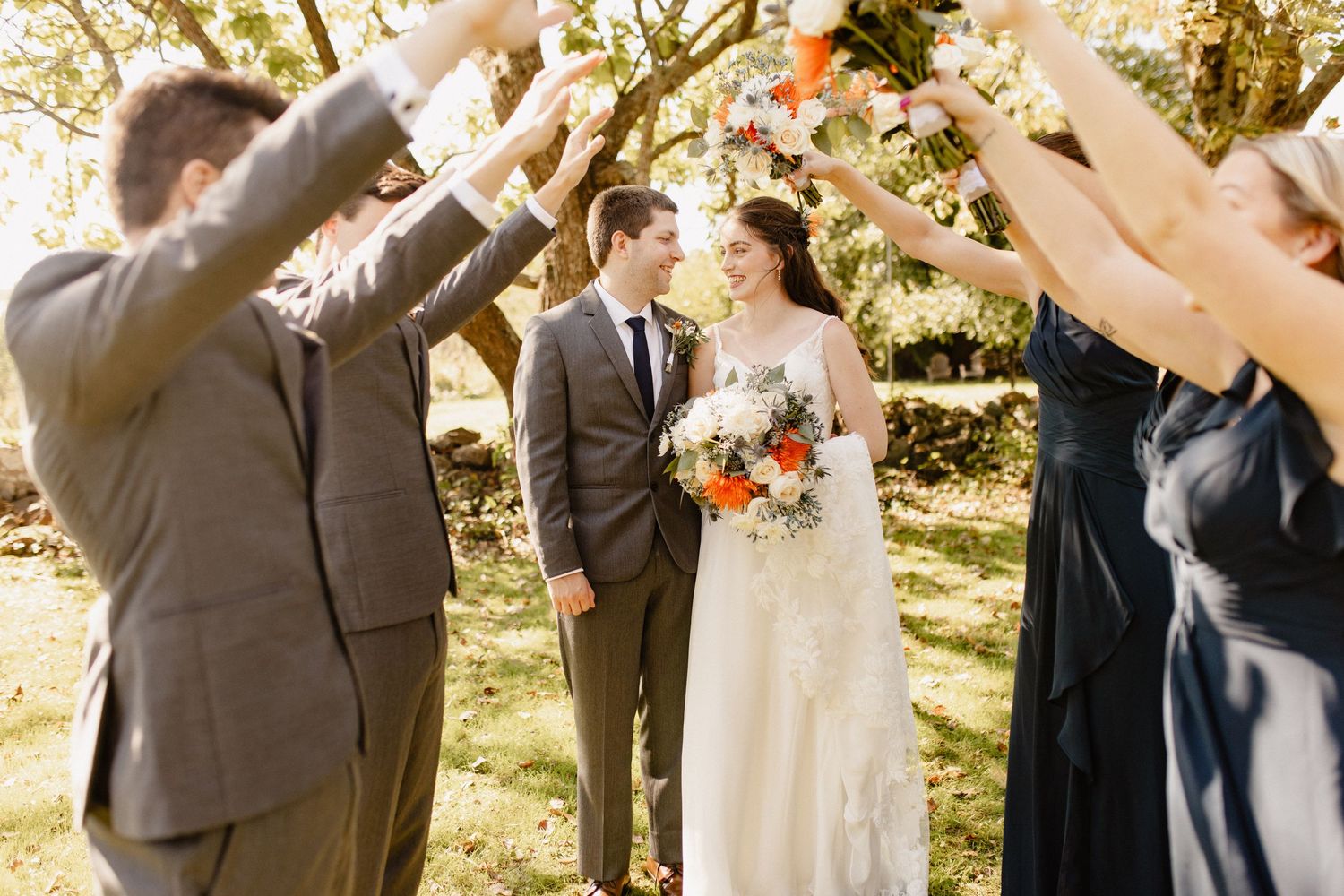 Wedding guests form a celebratory tunnel as newlyweds walk through on a sunny autumn day.
