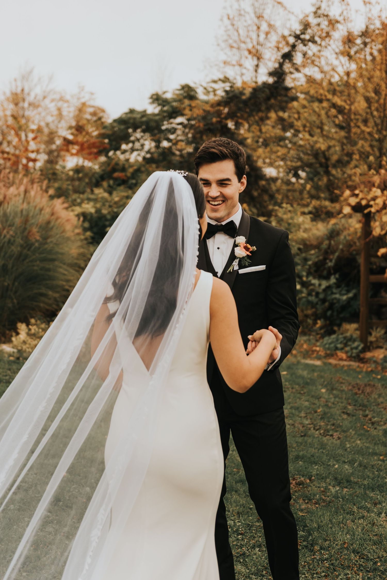 A bride and groom share a joyful moment outdoors during autumn with golden foliage in the background.