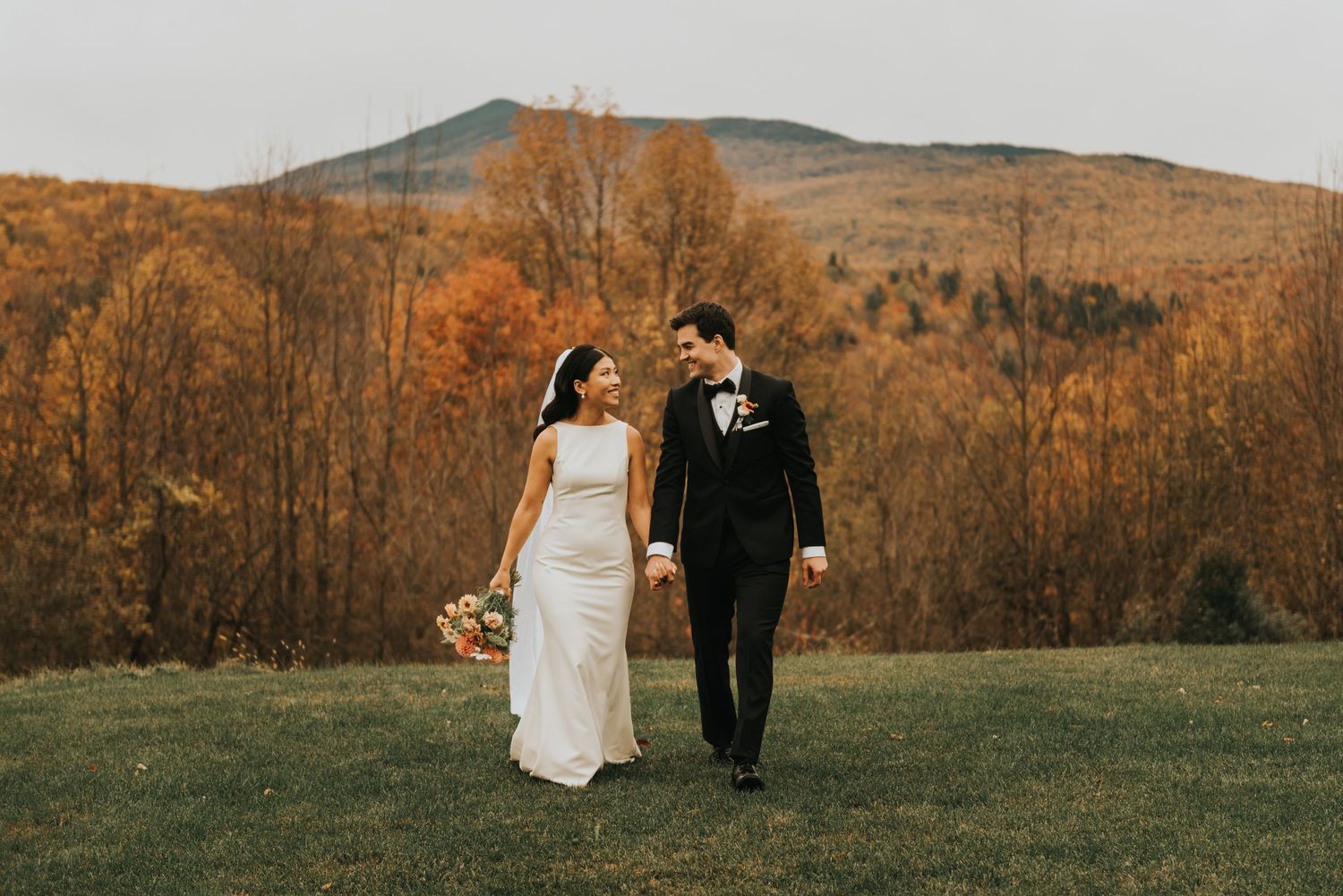 A couple strolls through a scenic fall mountainside setting with vibrant autumn foliage at sunset.