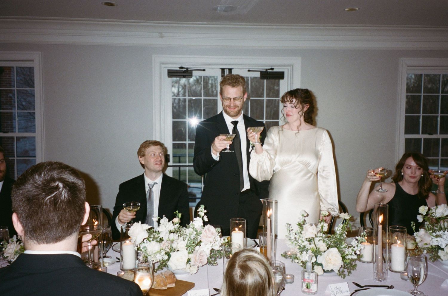 Wedding reception toast scene with guests seated at decorated tables during celebration dinner.