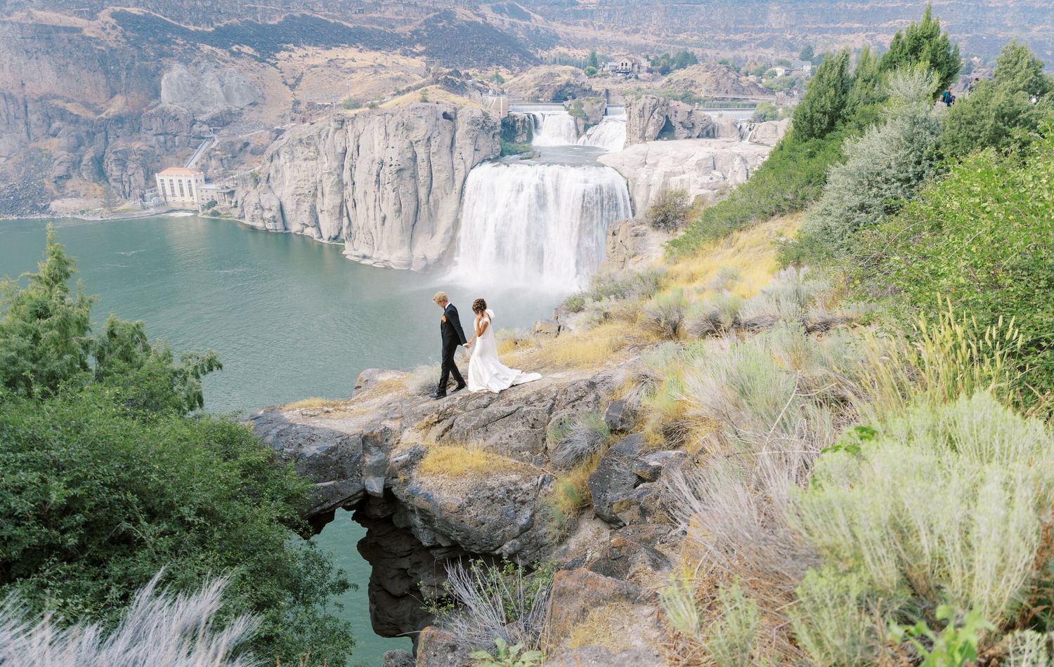 Scenic overlook of Shoshone Falls in Twin Falls, Idaho with cliffs and green foliage surrounding the waterfall.