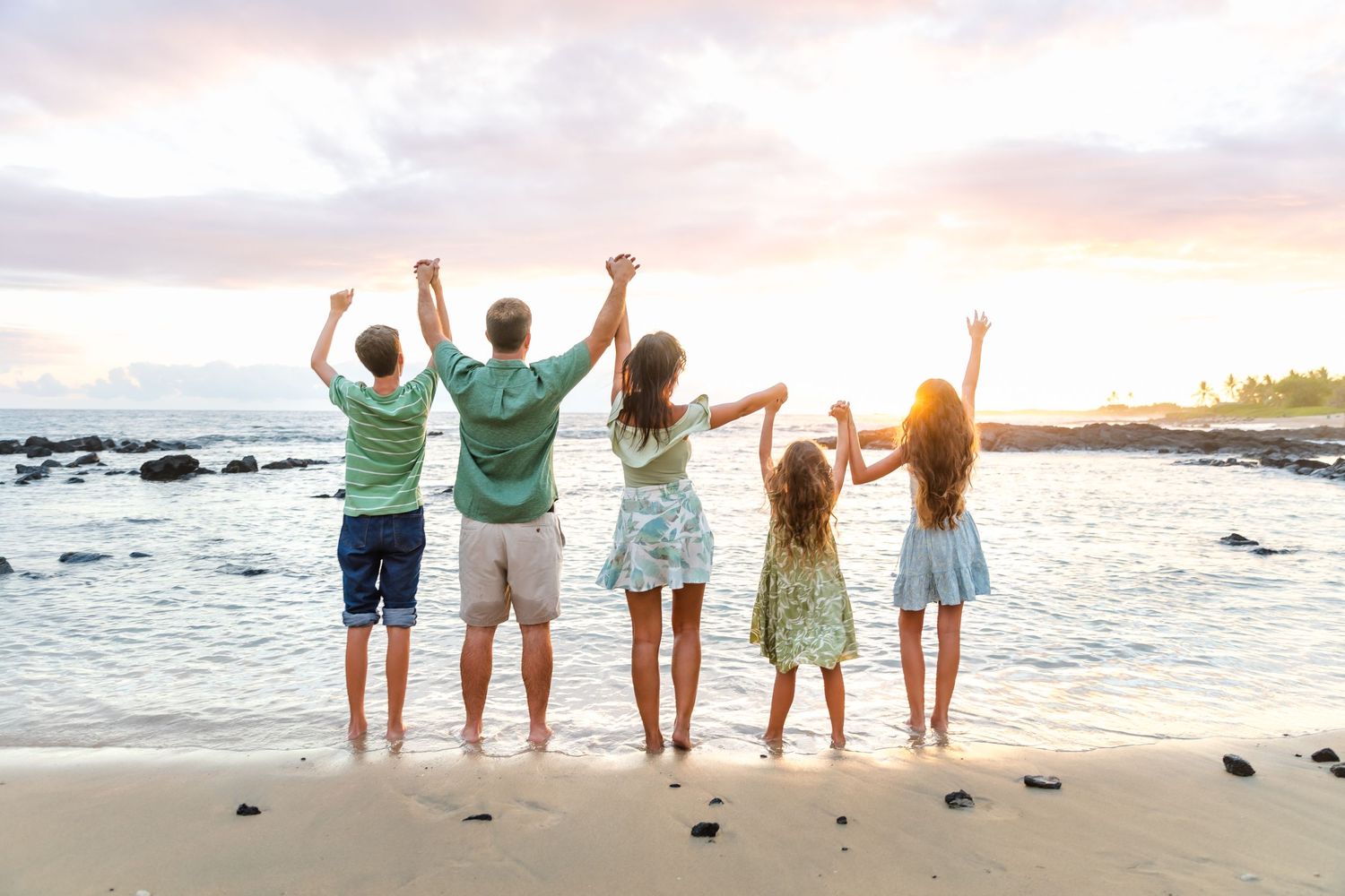 Family silhouettes celebrating with raised arms on beach at sunset.
