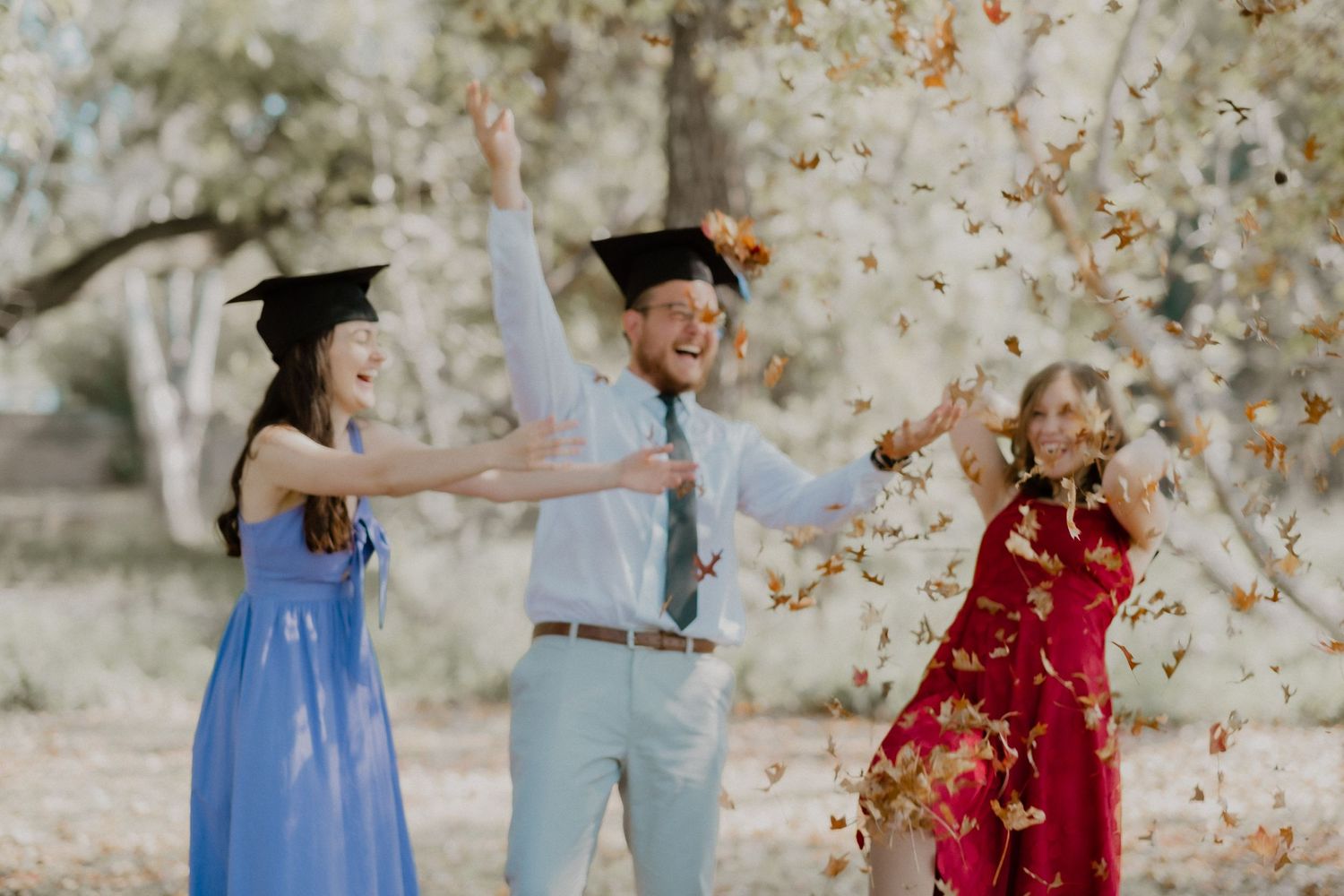 Three graduates celebrating with confetti in a joyful outdoor celebration.