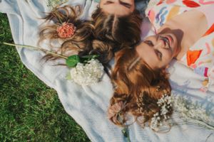 Photo of two women laying on a blanket with flowers on their hair.