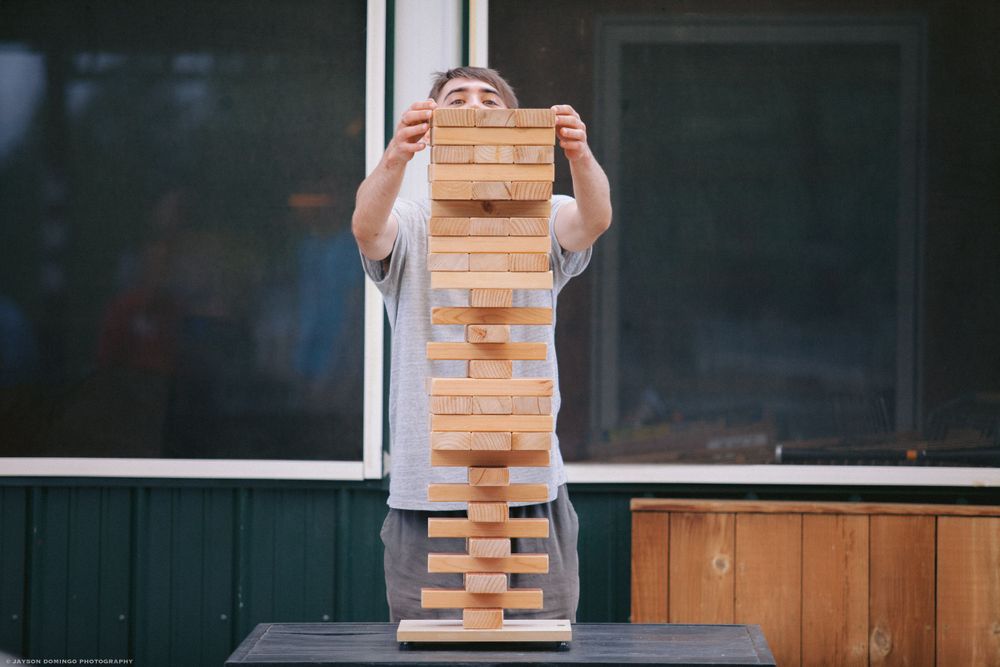 A person concentrates while playing a giant Jenga tower game outdoors.