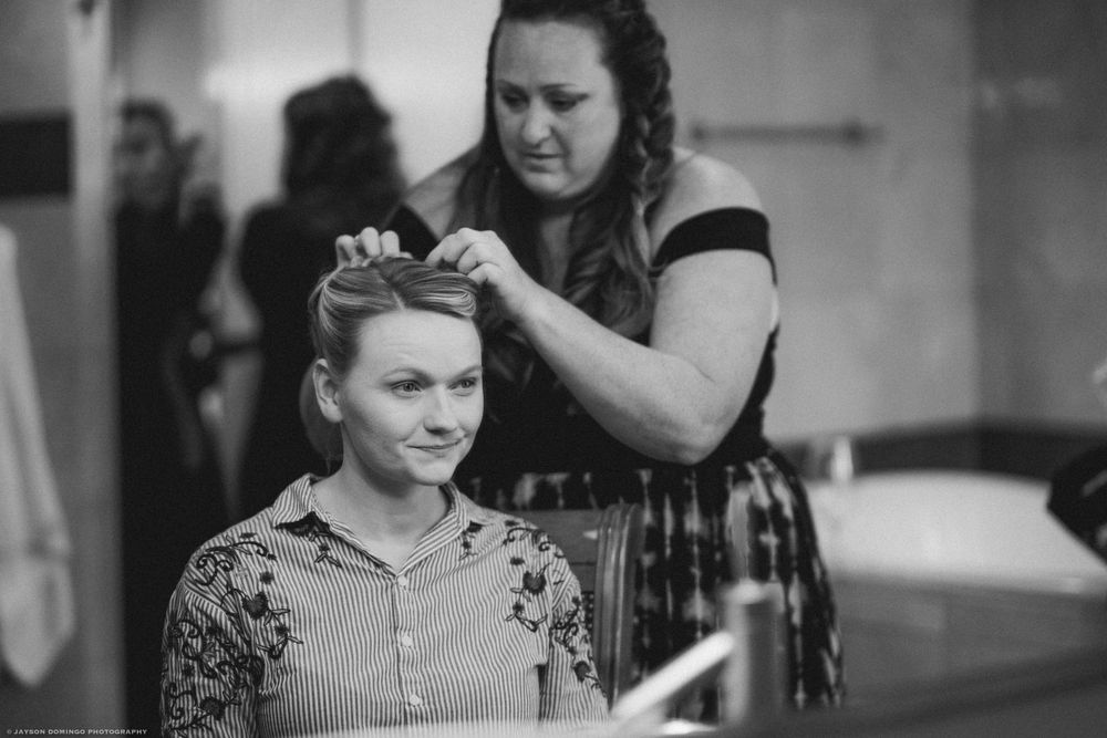 Black and white photo of wedding preparation as stylist works on formal hairstyle.