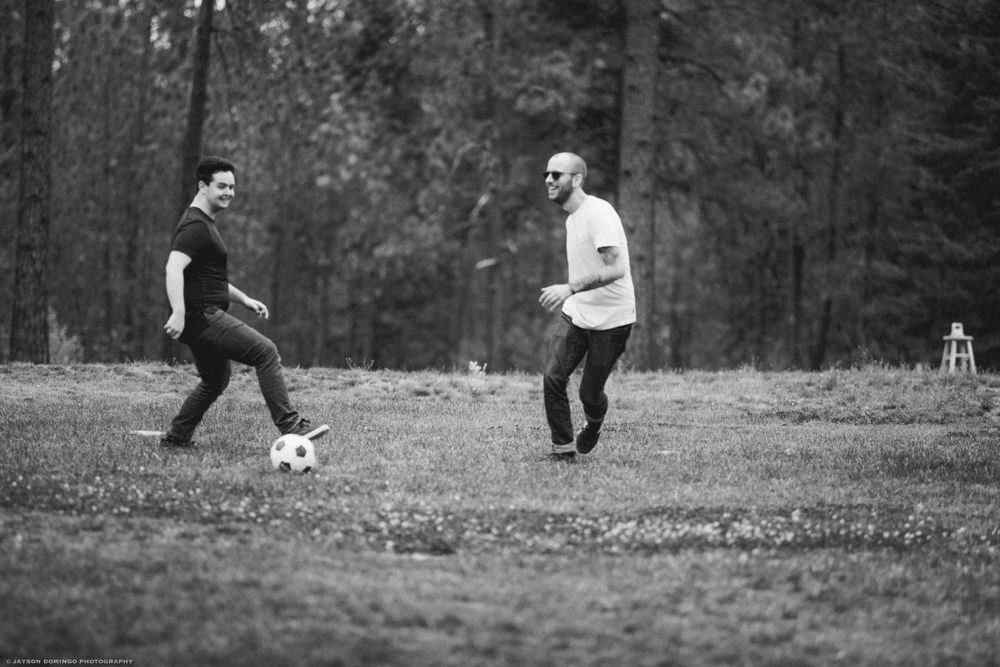 Two people playing soccer together on a grassy field in black and white photography.