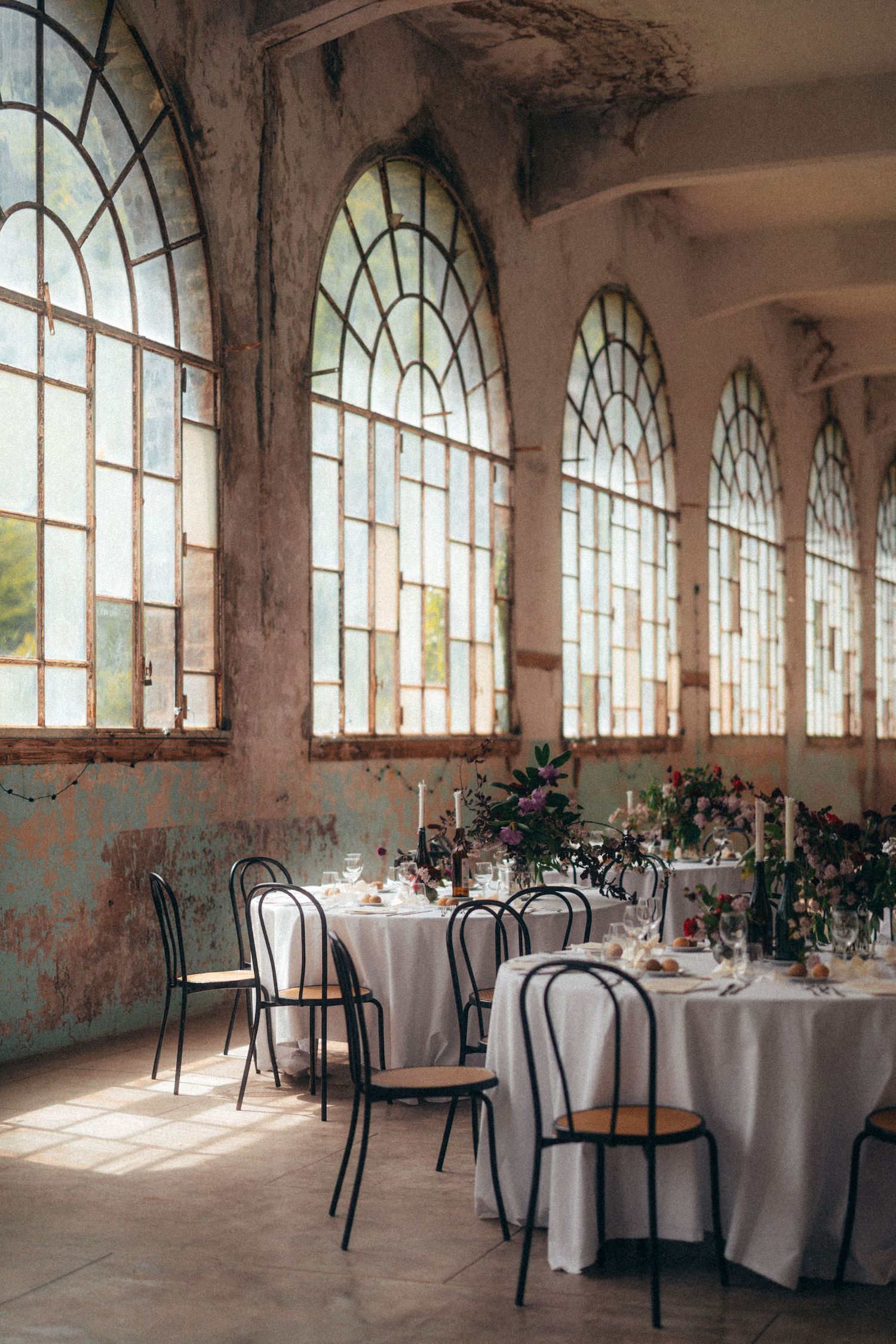 Elegant wedding reception in rustic venue with arched windows and white-draped tables.