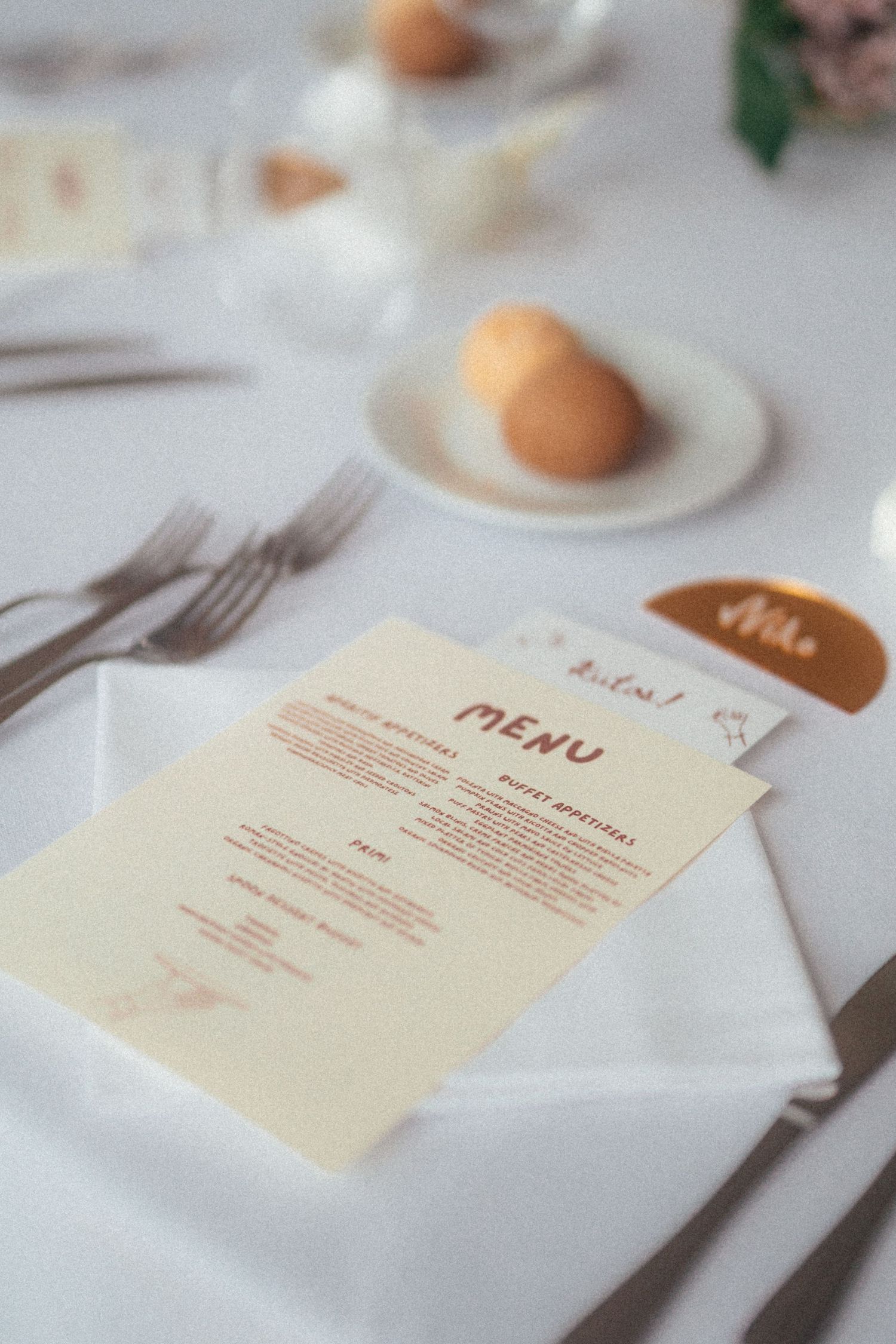 Elegant wedding table setting with a cream menu card, silverware, white napkin, and a small bread roll on a plate.