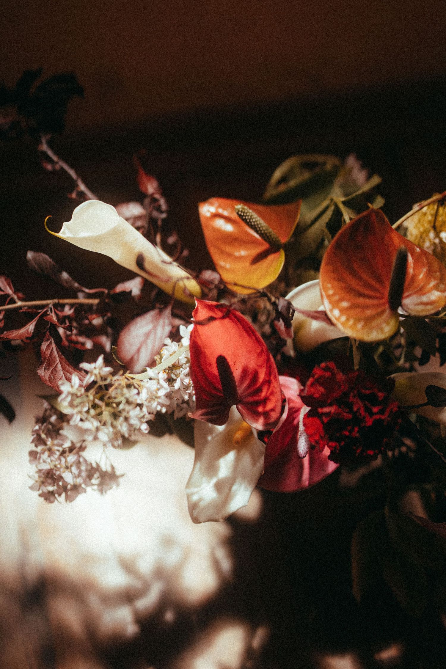 Close-up of rich bridal bouquet featuring red anthuriums, calla lilies, and autumn foliage in dramatic light.