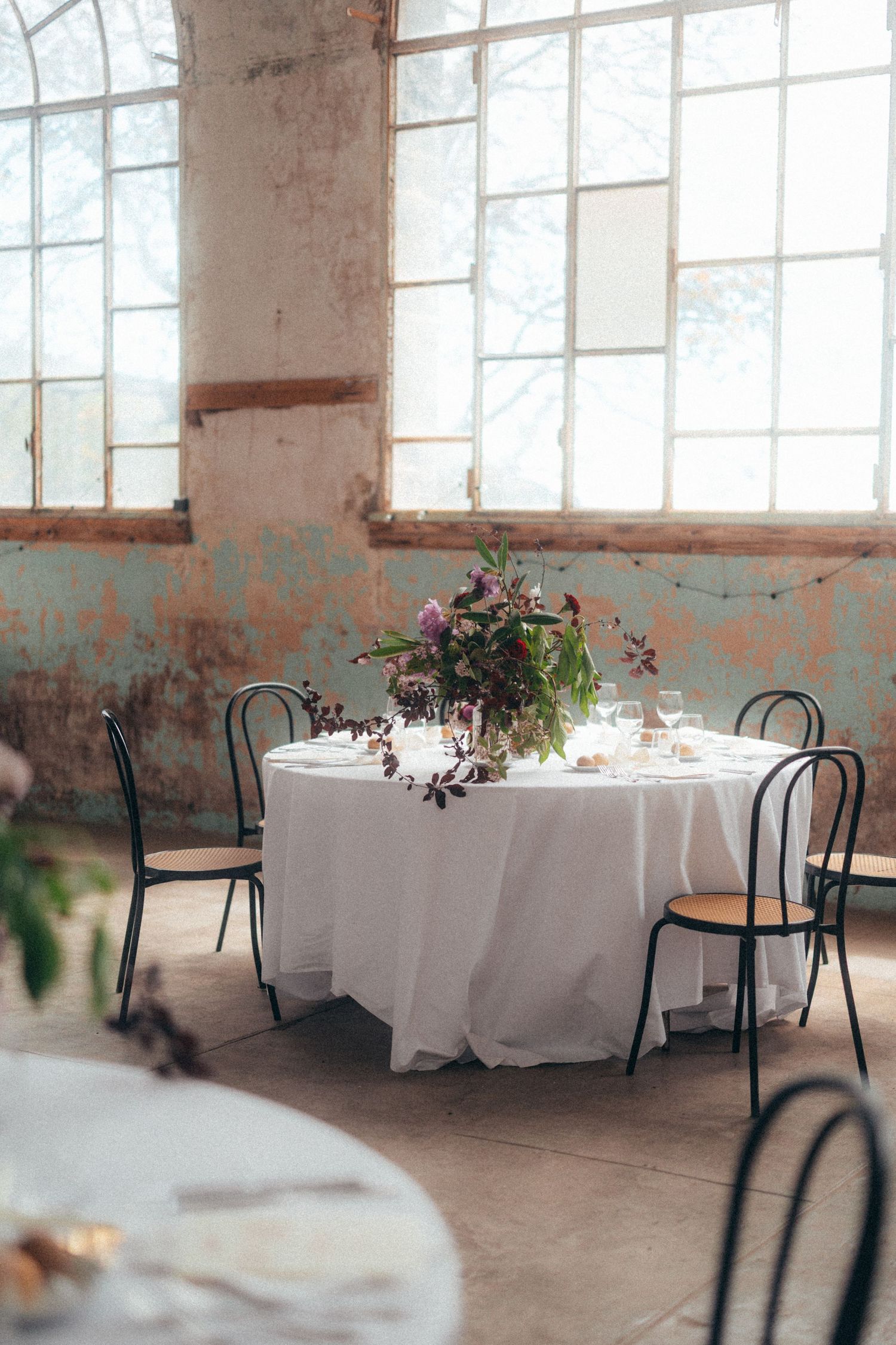 Elegant wedding reception table with white linen and floral centerpiece in a rustic industrial venue.