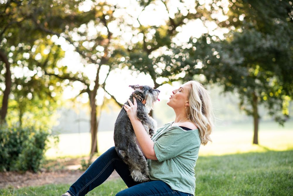 A person in a green shirt lifts and plays with their Australian Shepherd dog in sunlight at loose park kansas city.