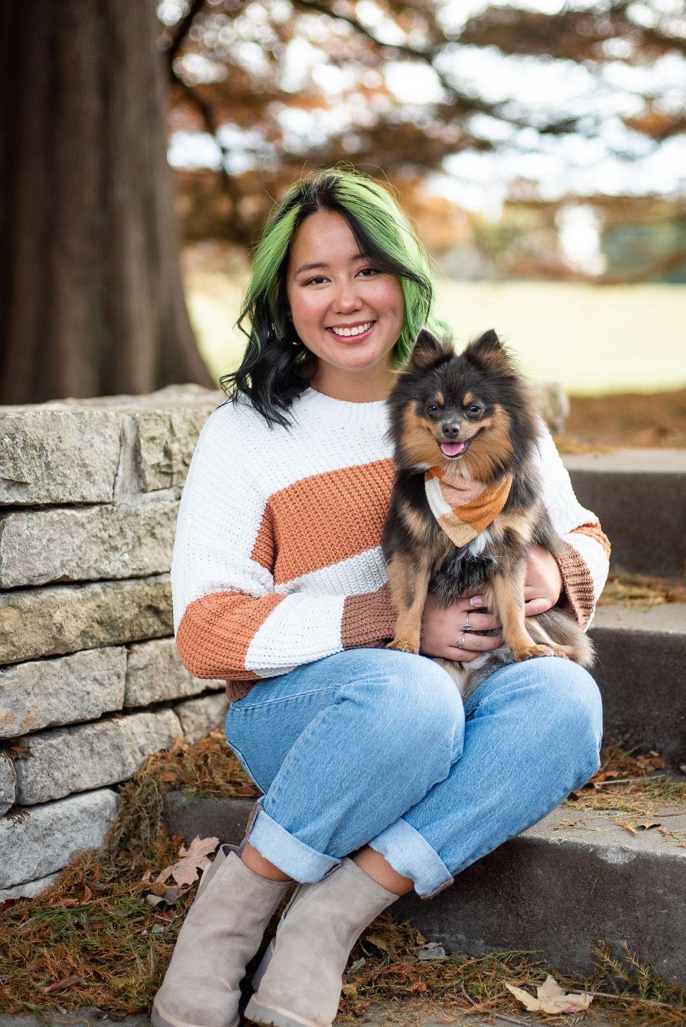 A person in a color block sweater sits on stone steps with their adorable Pomeranian dog on an autumn day.