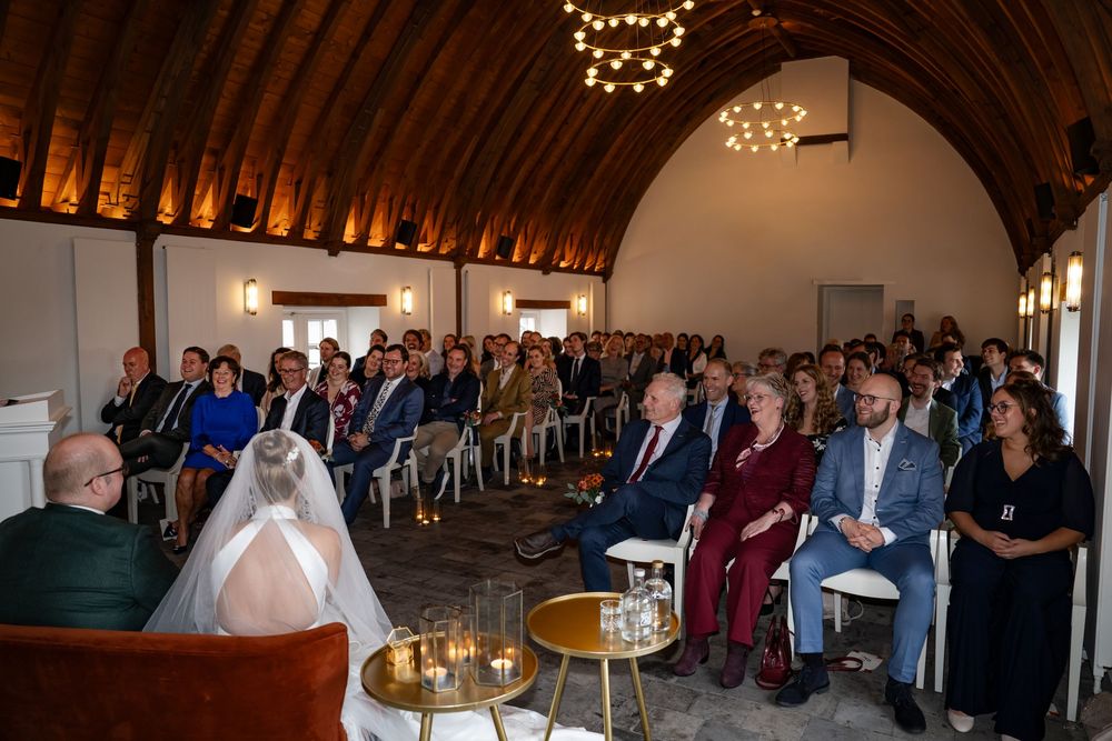 Lachende bruidsgasten en het bruidspaar tijdens de trouwceremonie in trouwlocatie kasteel Woerden.