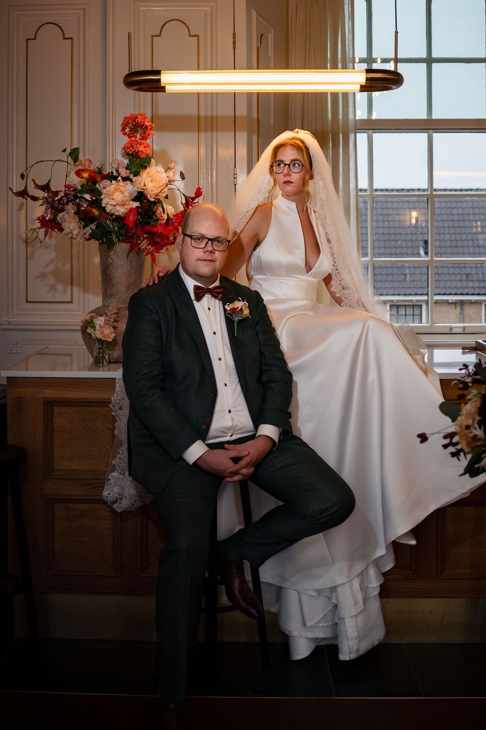 Bruid zit op de bar van trouwlocatie kasteel Woerden en de bruidegom zit ervoor op een kruk om te poseren voor hun trouwfoto.