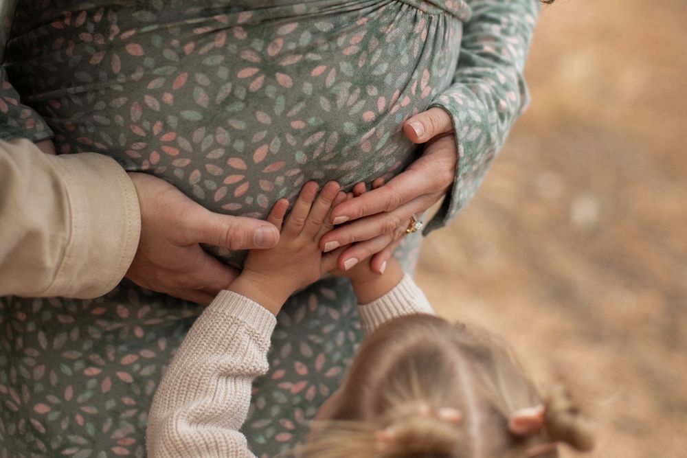 Tender moment captured as small hands reach up to touch a pregnant belly covered in a floral patterned dress.
