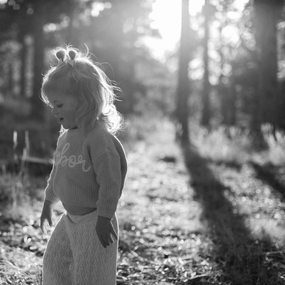 Black and white silhouette of figure in a sundress standing in sunlit forest with dreamy backlighting.
