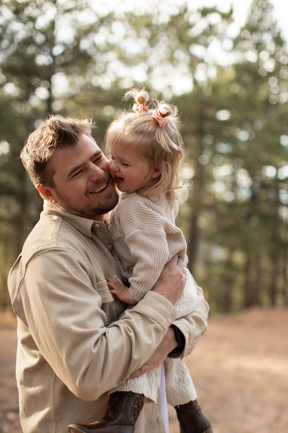 A tender moment shared between an adult and child hugging and laughing together in an autumn forest setting.