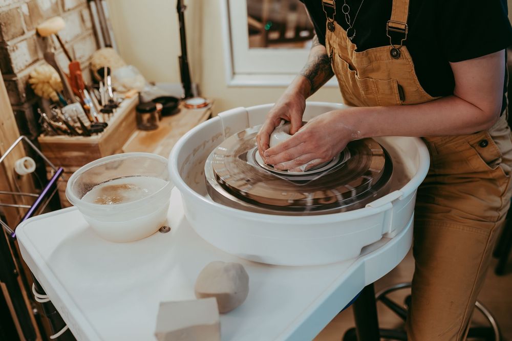 Artist working at pottery wheel with wet clay on a white table in a studio workshop setting. Whitney Popp, branding photography, Arizona.