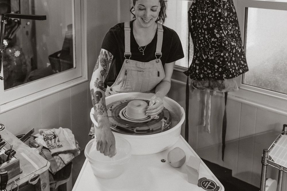 Artist is shaping clay on a pottery wheel in a bright studio workspace while wearing an apron. Whitney Popp, Arizona photographer, branding.