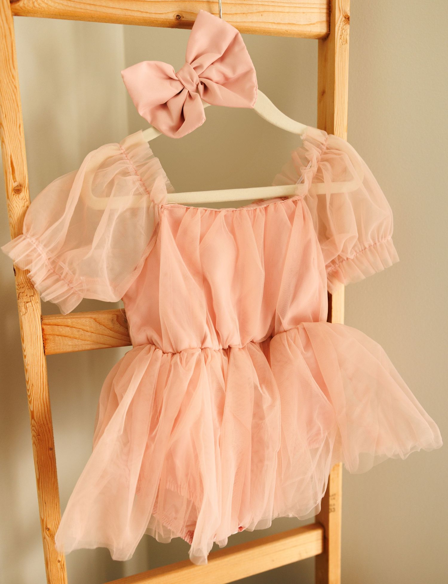 A delicate pink tulle ballet dress with puff sleeves and matching bow on a wooden hanger against a light background.