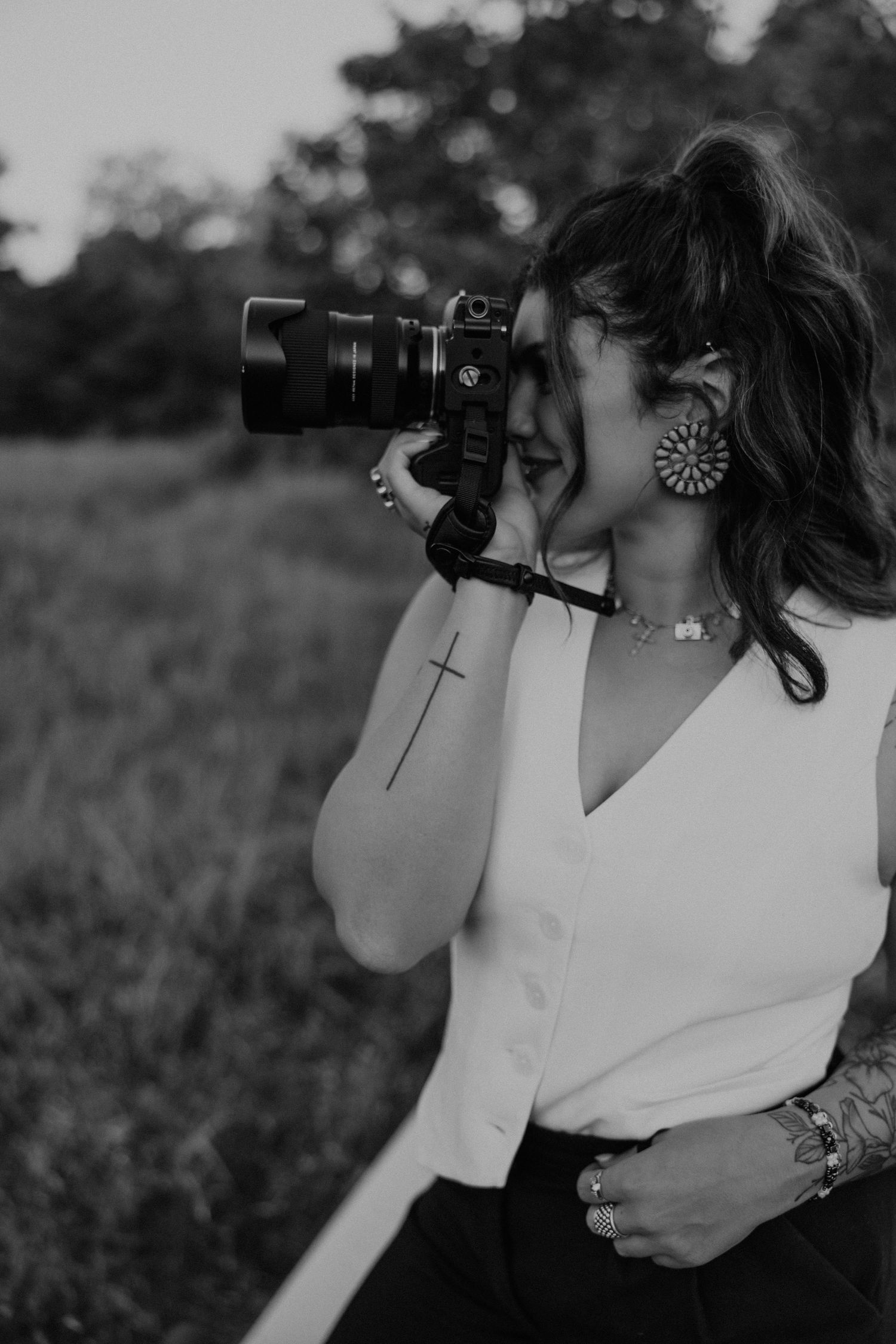 Black and white photo of a photographer using a professional camera in an outdoor field at dusk.