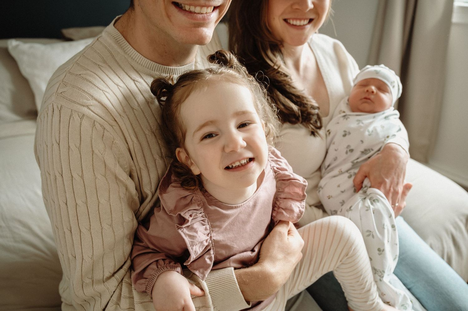 A heartwarming family moment captured on a cozy bed with cream-colored sweaters.