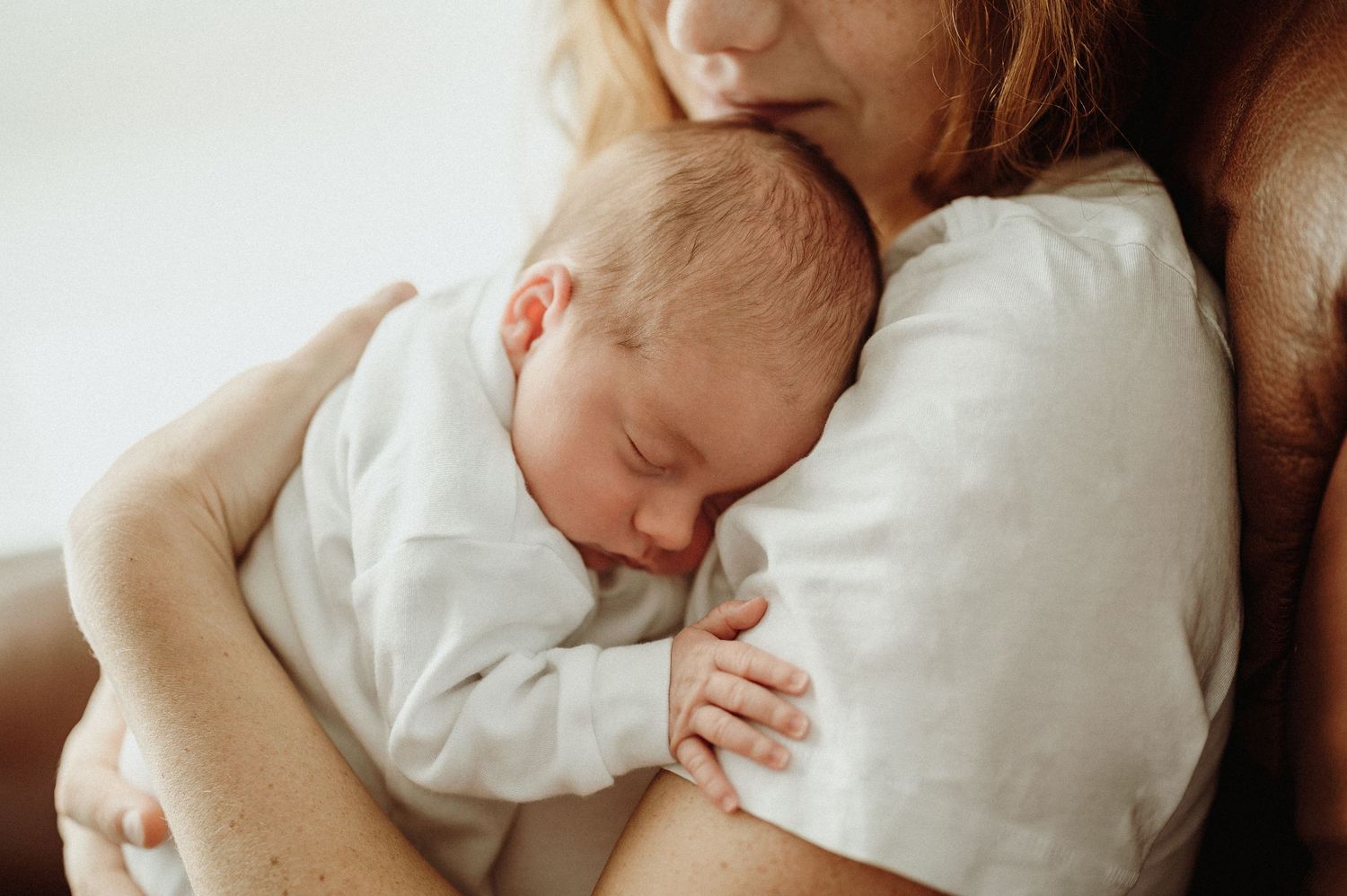 A sleeping newborn in white clothing rests peacefully against a caregiver.