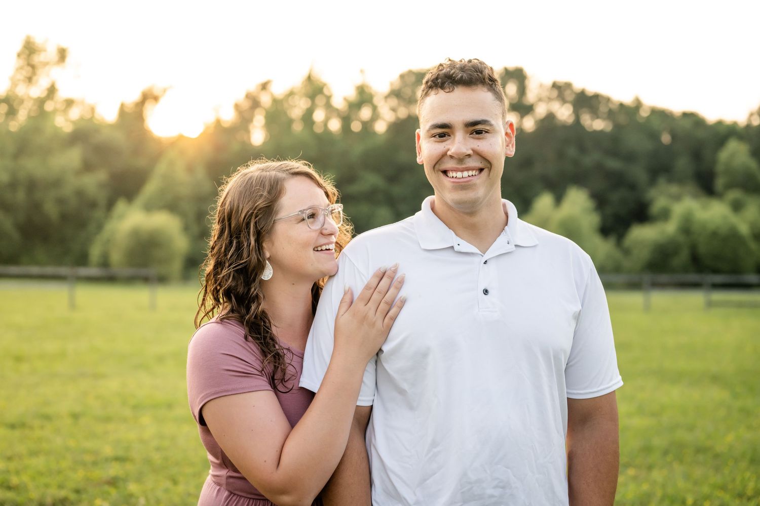 A couple shares a joyful moment together in a sunlit meadow during golden hour.