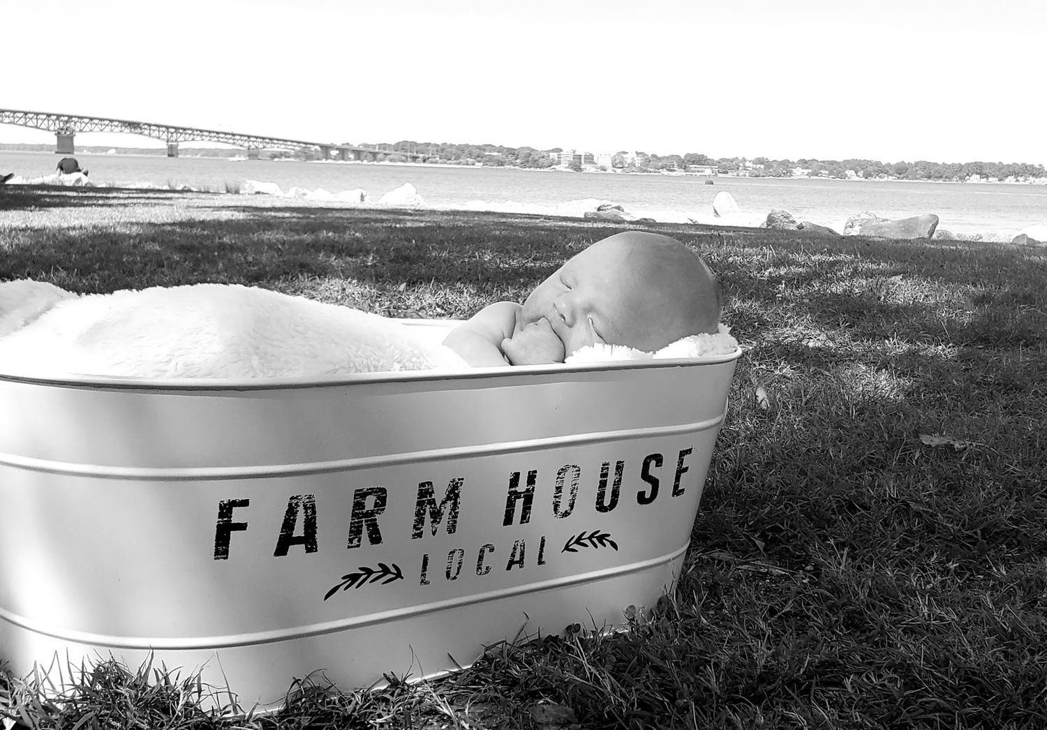 1 month old milestone image in black and white of baby boy with the york river in the background showing the George P coleman bridge