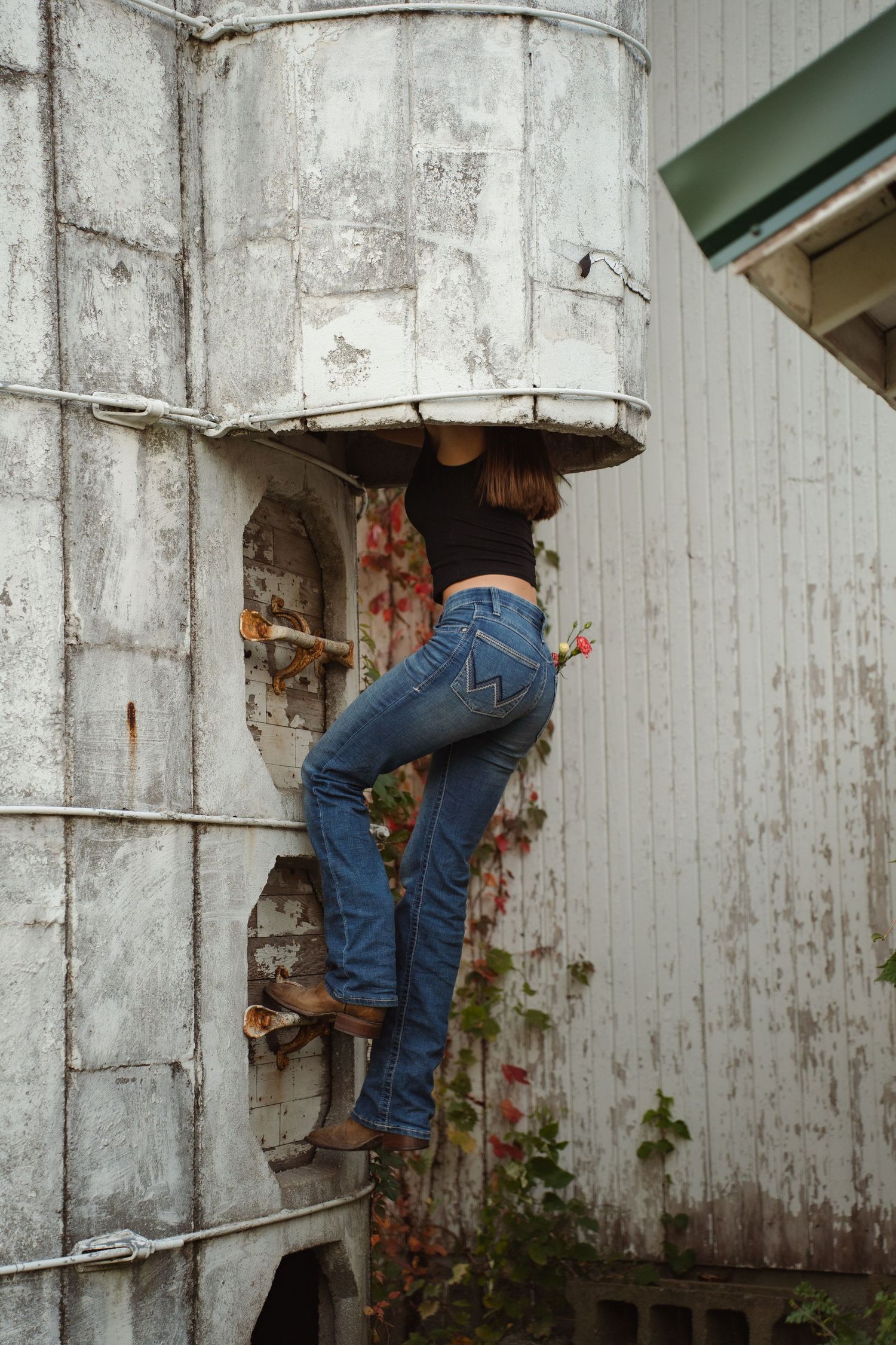 Person climbing weathered white silo structure in casual denim outfit.