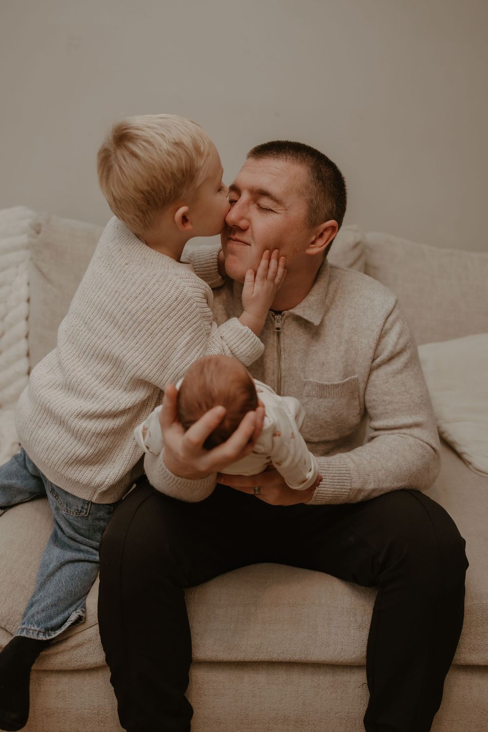 Toddler sibling shares sweet moment with Dad and newborn baby sister.