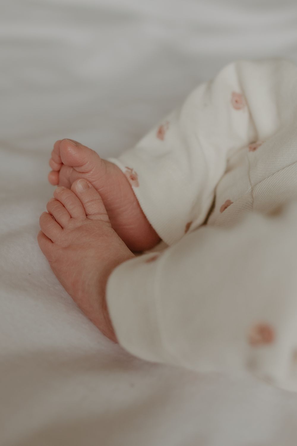 Tiny baby feet peek out from white clothing against soft bedding.