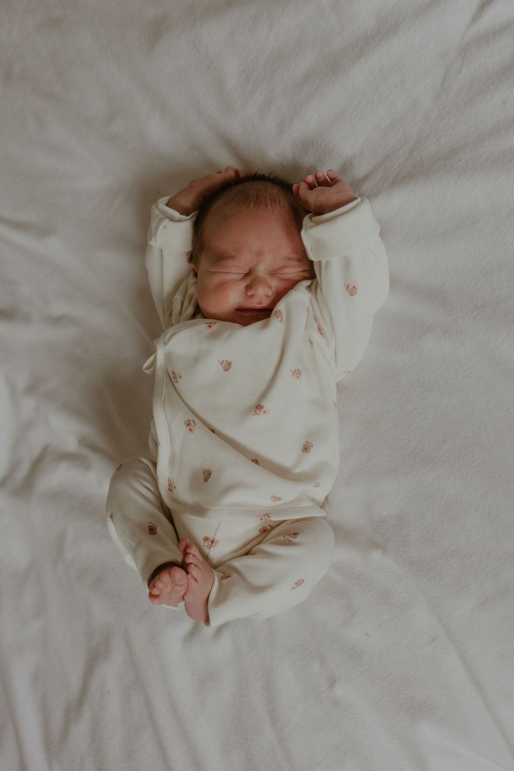 Newborn baby sleeping peacefully in white onesie with delicate pattern.