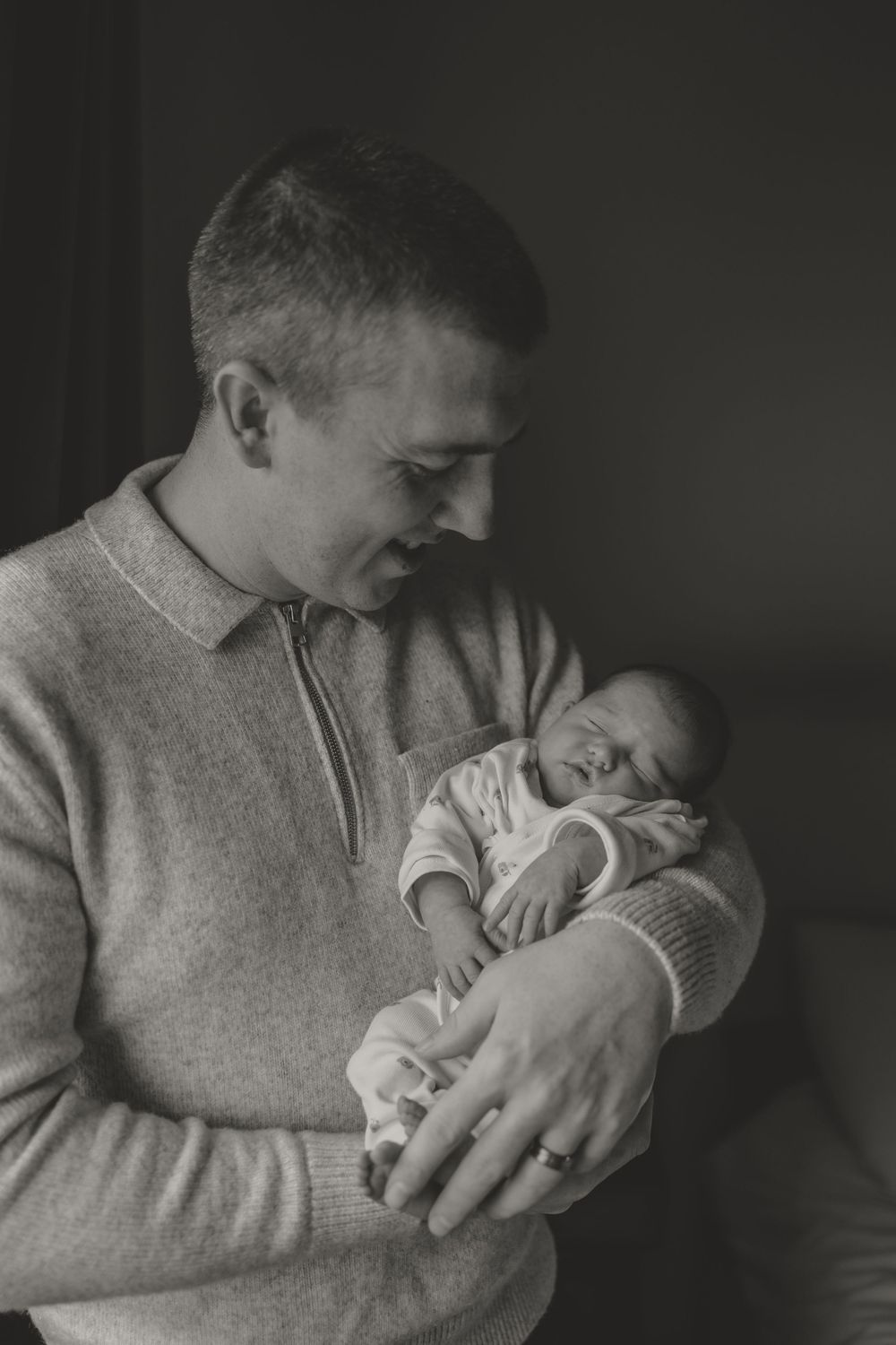 Dad tenderly holds sleeping newborn in intimate portrait.